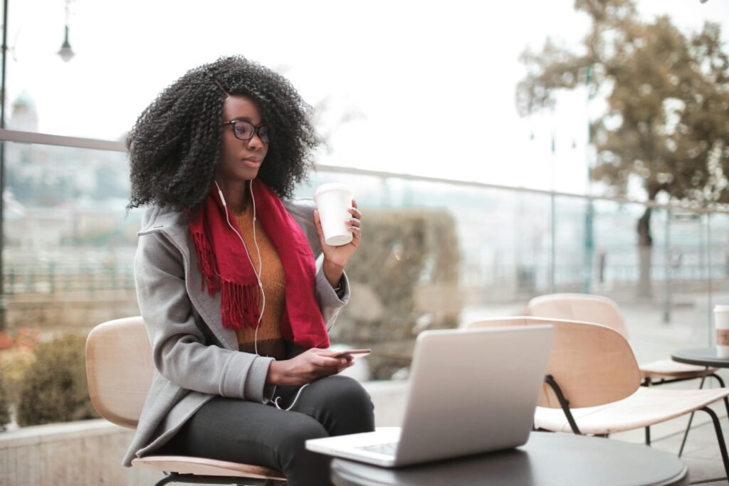 Confident woman working remotely in an outdoor café, sipping coffee and using a laptop.